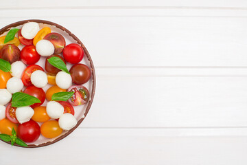 Baby mozzarella, cherry tomatoes and basil salad on white background top view with copy space. Caprese salad.