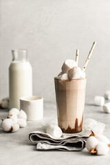 Milkshake with chocolate, marshmallow topping and straws on light background. Composition with ingredients and cotton flowers