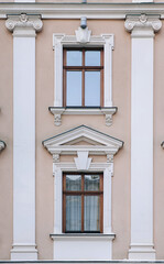Two windows on the facade of a beige house in the central historical part of the city. Beautiful decorative architecture with reliefs on white cornices and pilasters in Lviv, Ukraine.
