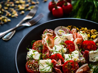 Tasty salad - prosciutto di Parma, feta cheese, cherry tomatoes, sprouts and fresh, green vegetables on black wooden table
