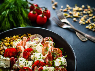 Tasty salad - prosciutto di Parma, feta cheese, cherry tomatoes, sprouts and fresh, green vegetables on black wooden table
