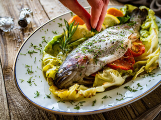 Roast trout with potatoes and tomatoes on green cabbage leaves served on wooden table