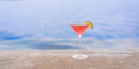 Glass with Cosmopolitan cocktail on the edge of the pool in a resort hotel - obrazy, fototapety, plakaty
