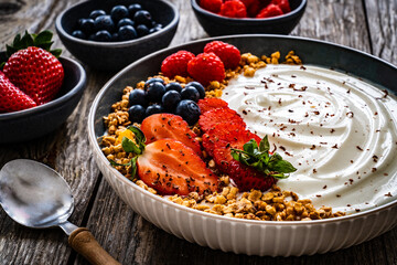 Yogurt with strawberries, blueberries, raspberries and muesli in bowl on wooden table