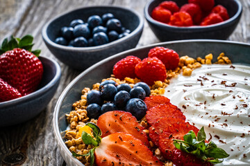 Yogurt with strawberries, blueberries, raspberries and muesli in bowl on wooden table