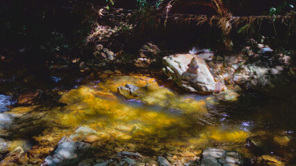 pile of stones lit by the sun's rays, on the bank of a clear stream running over the rocks.