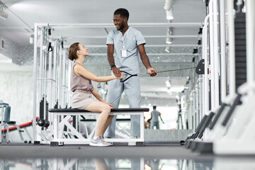 Side view portrait of smiling medical therapist assisting young woman in rehabilitation clinic