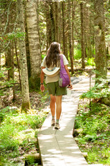 Woman hiker walking on boardwalk through a path in the woods.