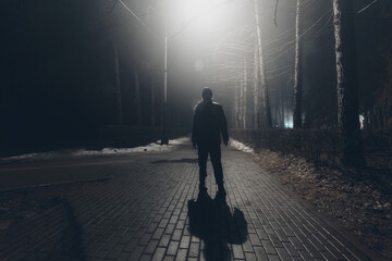 Sad man alone walking along the alley in night foggy park