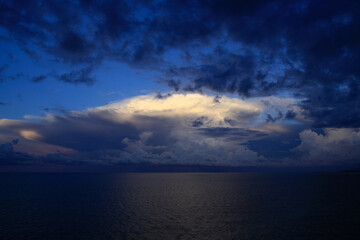 Obraz na płótnie Canvas Panoramic view of ocean waters horizon line with dramatic cumulus thunderstorm cloudscape in blue sky background.