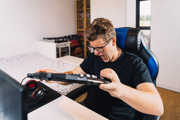 young blond man banging on the keyboard in anger at losing a video game on his computer. Young...