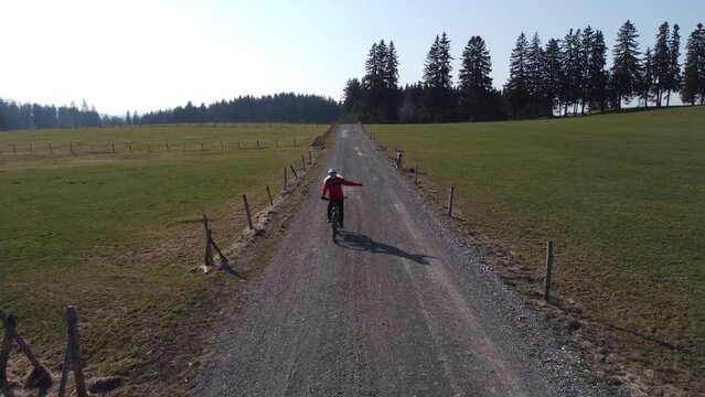 Video mit einer Drohne von einer Fahrradfahrerin auf einem Feldweg in Bayern, die in die Kamera winkt