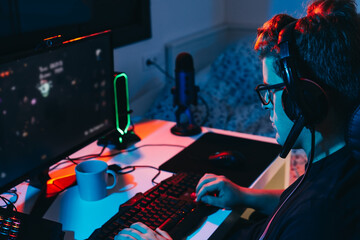 Young man addicted to online video games, playing on a computer. Young gamer illuminated with coloured lights.