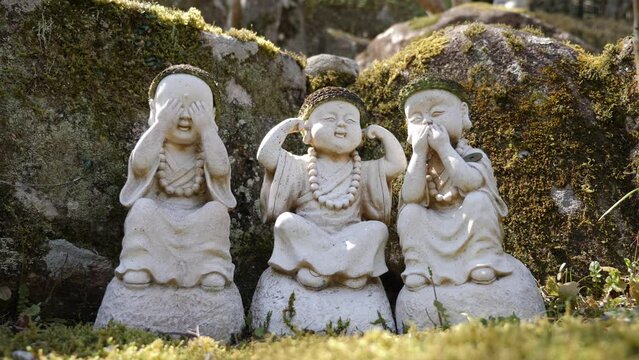 Three stone figures of buddha acting like three wise monkeys Mizaru, Kikazaru, Iwazaru. Covers his eyes, and sees no evil, covers his ears, and hears no evil and covers his mouth, and speaks no evil