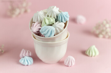 Airy small meringues of early flowers in a white double cup on a pink background. selective focus
