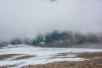 Dramatic landscape with people inside cloud above motley mountain valley. Tourists in cloud above multicolor valley. Low cloud on stone hill with snow. Awesome high mountain scenery in low clouds.
