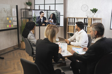 Team of diverse four multiethnic businesspeople having video meeting in boardroom at office indoor looking at African business lady and Caucasian man, using smart video technology to communicat