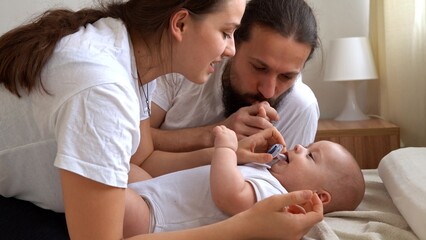 Fototapeta premium Woman And Man Holding Newborn. Mom, Dad And Baby On Bed. Close-up. Portrait of Young Smiling Family With Newborn On Hands. Happy Marriage Couple On Background. Childhood, Parenthood, Infants Concept