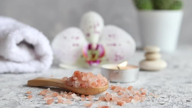 Pink himalayan salt close-up on a wooden spoon with candle, orchid flower and towel. Beauty and spa concept. Selective focus