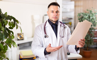 Portrait of confident young male doctor reading documents at medical office