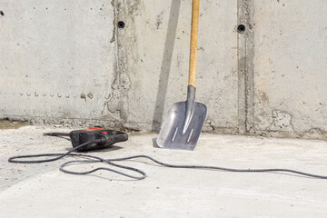 impact drill with a flat chisel on a monolithic ceiling, a shovel stands against the wall
