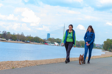 Mother and her teen girl walking with pinscher dog by the lake.Concept of relationship between...