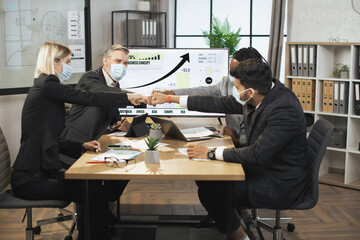 Multiethnic business people, fists bump, celebrating corporate achievements, while meet in office boardroom with big wall digital screen. Teamwork, common decision, share advance concept.