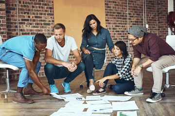 Difficult becomes ease when you have a great team. Shot of a team of entrepreneurs collaborating sitting on the floor in a modern office.