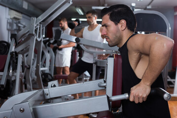 Portrait of athletic man during workout with power exercise machine in gym club