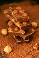  chocolate with nuts stack close-up on a black background.Broken chocolate texture.Chocolate with hazelnuts and cocoa powder.Desserts and sweets.Milk chocolate with nuts . 
