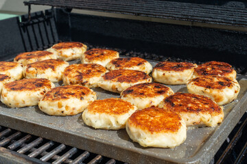 A tray of cooked round salt cod fishcakes is prepared on a barbeque. The savory, potato, salt codfish, and butter mixture are shaped into small patties and fried in butter until golden brown.