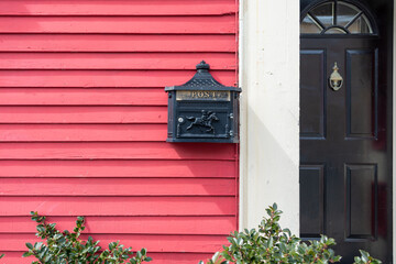 The exterior wall of a colorful red wooden clapboard siding house with a black metal mailbox, and a...