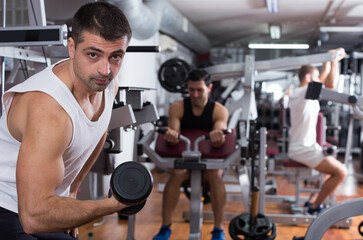 Fototapeta na wymiar Concentrated sporty guy during workout in gym with dumbbells