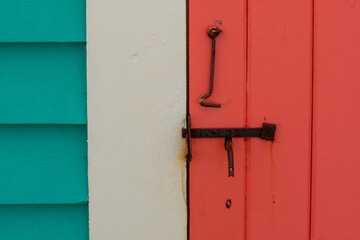 A vibrant teal green house with cream color trim and a vibrant orange shutter door. The closed door...