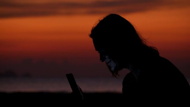 Mother holds smartphone and takes pictures daughter at dramatic sunset on beach. Friendship, love and happy family forever on summer vacation