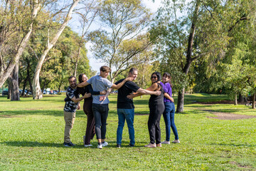 Multi ethnic family group walking arm in arm in a park, looking at the camera smiling, happy attitude. Family, group, teamwork, friendship concept