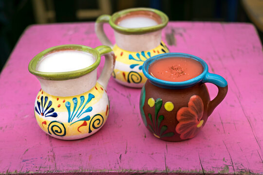traditional Mexican earthenware jars with fruit-flavored pulque, on an old Mexican pink table.