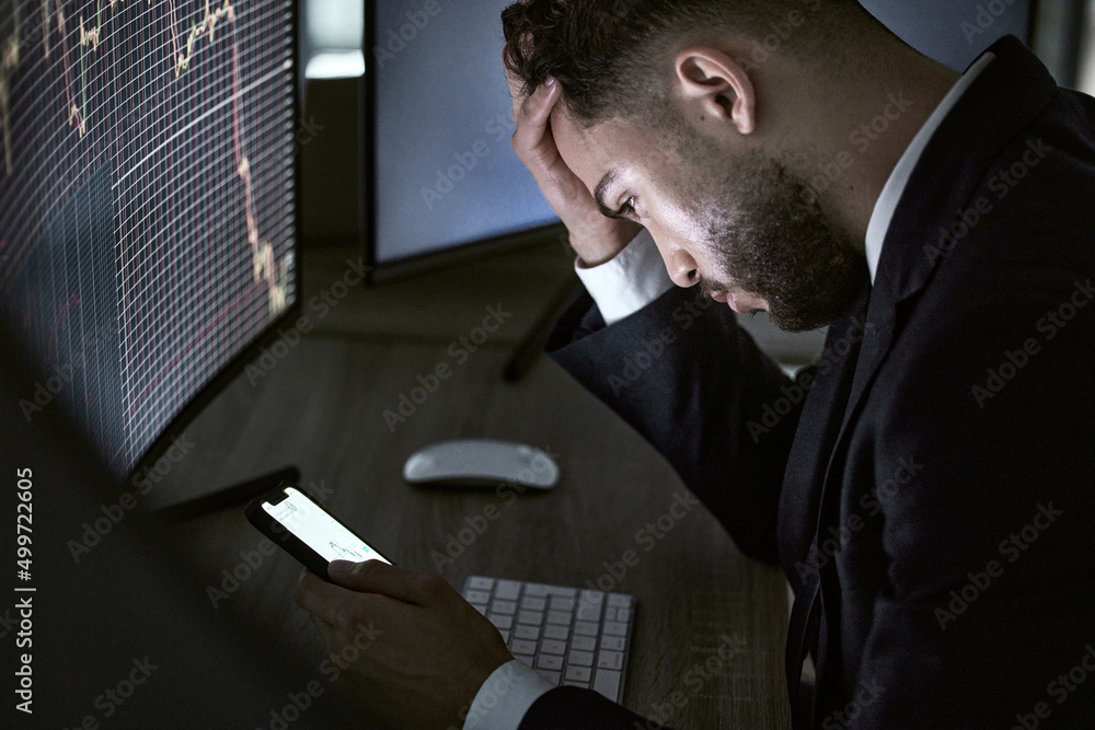Poster In desperate need of some good news. Shot of a young trader using his smartphone while monitoring the stock market.