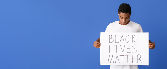 Sad African-American teenage boy holding poster with text BLACK LIVES MATTER on blue background....