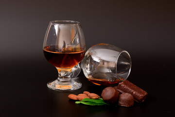 Two glasses of cognac, chocolates, almonds and mint on a black background.