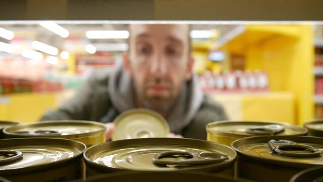 Close-up of many beautiful cans of olives on a supermarket shelf and a man takes one