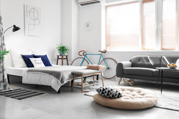 Interior of light room with comfortable bed, sofa and modern bicycle