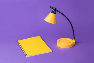 A table lamp with a yellow notebook on a purple background.