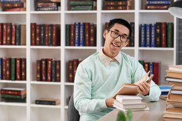 Male Asian student reading book at table in library