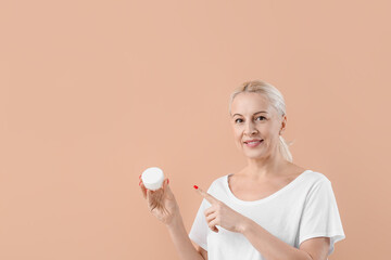 Mature blonde woman pointing at jar of cream on beige background