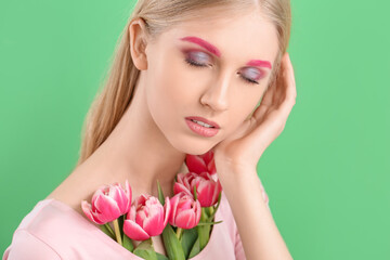 Woman with creative makeup and beautiful tulips on green background
