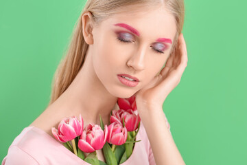 Fototapeta premium Woman with creative makeup and beautiful tulips on green background