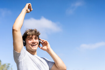 Young man listening to music outdoors with bluetooth headphones. Expression of happiness, winning...