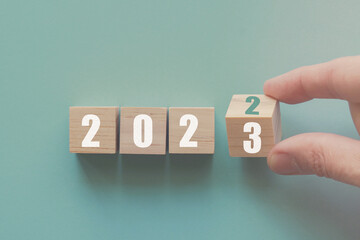 Hand flipping over wooden block of 2022 to 2023, New Year Resolutions, business concept