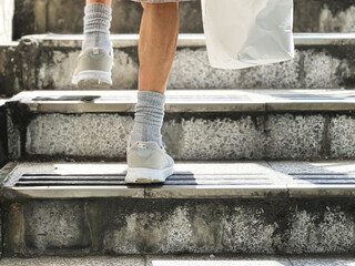 紙袋を持って階段を登る高齢女性の足元